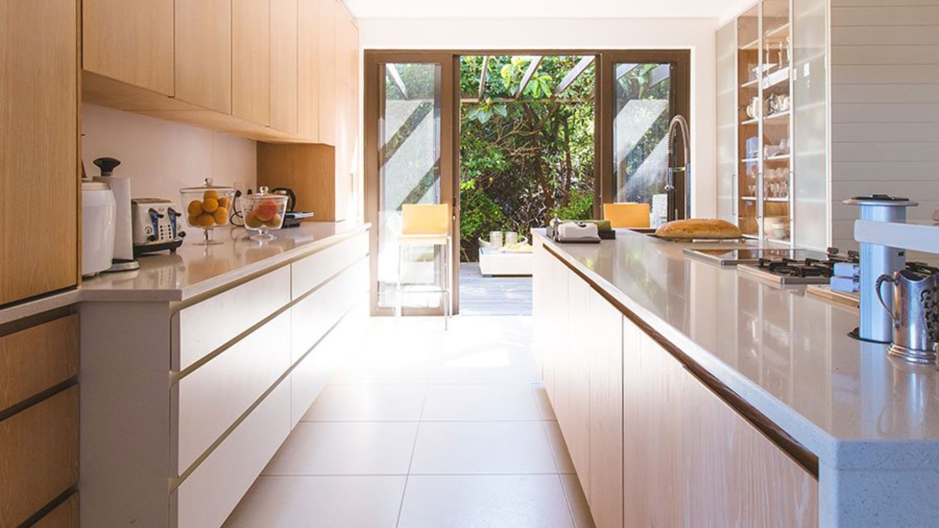 Cuisine moderne avec îlot central et grandes portes vitrées donnant sur une terrasse extérieure verdoyante